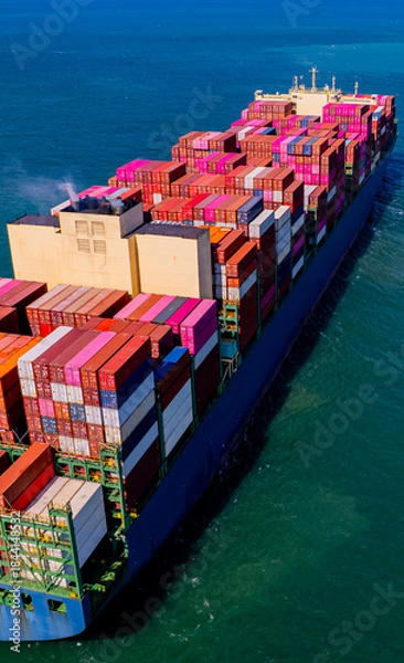 Fototapeta container ship, fully loaded with goods, sails out to sea, delivering products to various locations