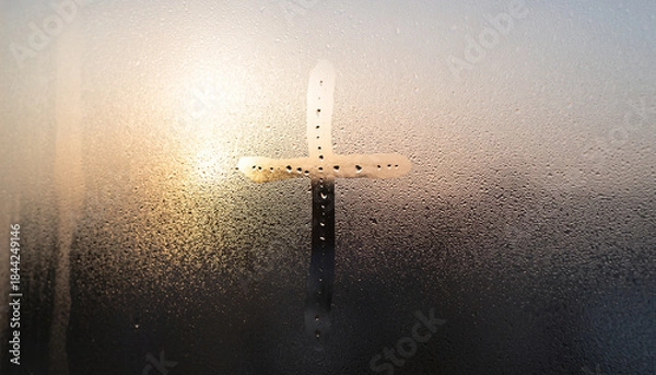 Obraz A Christian cross drawn on a steamy window with sunlight in the background.