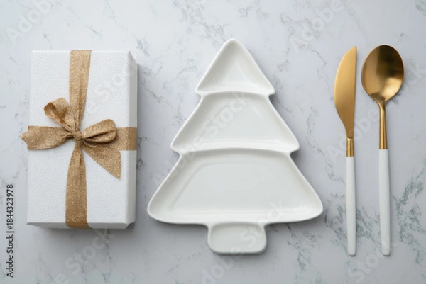 Fototapeta A festive holiday table setting featuring a ceramic Christmas tree plate with ribbon and pine sprig, surrounded by gifts