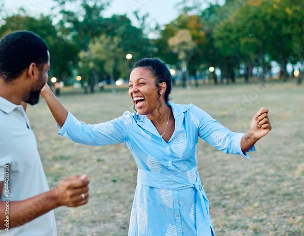 Fototapeta Happy young black couple, portrait of a beautiful woman with her husband dancing or swinging and holding hands in park outdoors