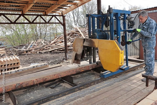 Fototapeta Wood processing at a sawmill. A professional carpenter uses a machine for sawing wooden planks. Lumber is in stock. Production concept.