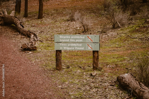 Fototapeta Wooden information board with symbols about bicycles and fires are prohibited along the walking path outdoor in the forest of Wilpena Pound in the Outback of Australia.