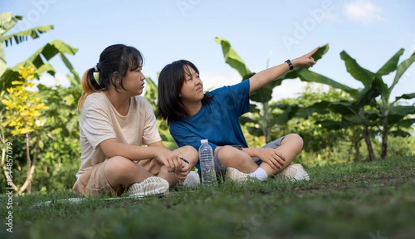 Obraz Two girls relaxing on grass outdoors, chatting after playing badminton.