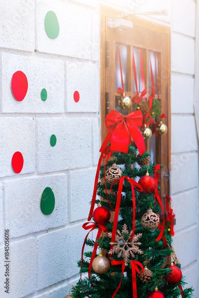 Fototapeta Festive Christmas tree decorated with red ribbons, baubles, and ornaments beside a window, creating a warm holiday atmosphere.