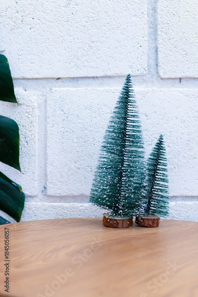 Fototapeta Minimal Christmas decoration with small artificial pine trees on wooden table and white brick wall background, festive holiday and winter concept.