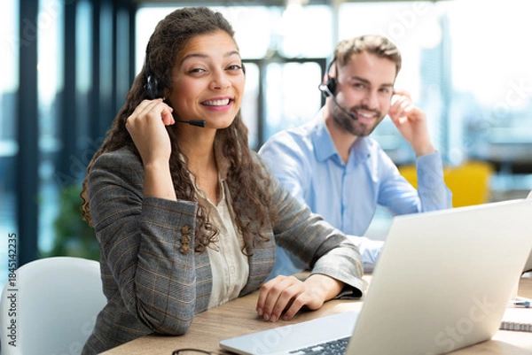 Obraz Customer service representatives engaged in professional work using headsets and laptops.