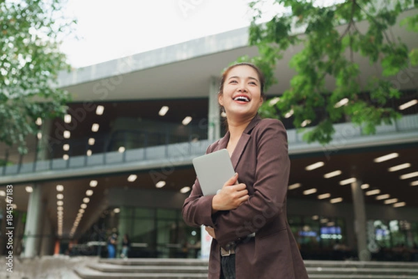 Fototapeta Young businesswoman smiling cheerful holding digital tablet outside modern building