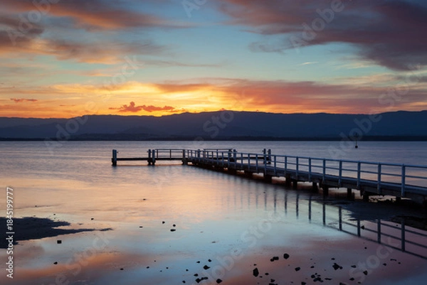 Fototapeta Boonerah Point jetty under a beautifully vibrant sky looking west to the mountains on Lake Illawarra, NSW, Australia.