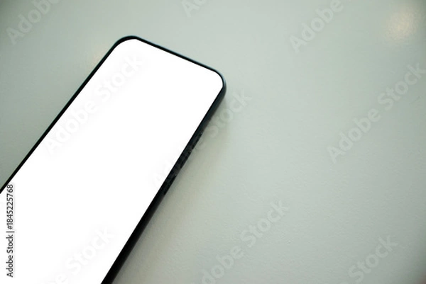 Fototapeta A smartphone is placed on a minimalist white table, copy space.