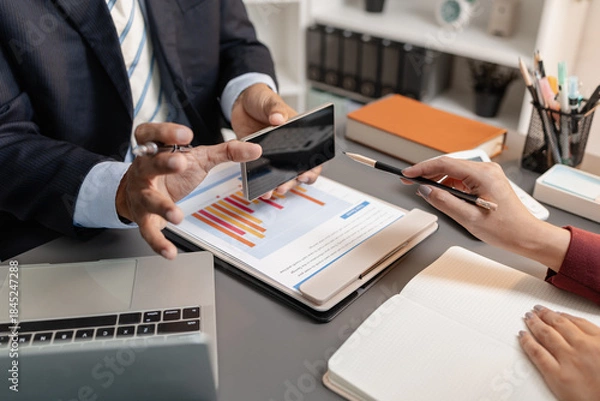 Obraz A collaborative startup meeting showing professionals reviewing financial charts and discussing strategic ideas in a modern office setting.