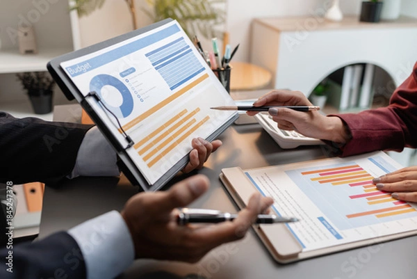 Obraz A collaborative startup meeting showing professionals reviewing financial charts and discussing strategic ideas in a modern office setting.