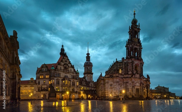 Obraz Evening view of Dresden Cathedral and historic buildings at Theater Square with illuminated baroque architecture, dramatic cloudy sky, and wet reflections in the old town of Saxony, Germany