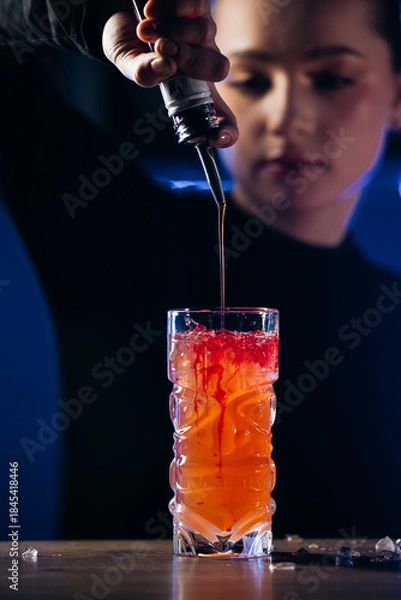 Obraz Female bartender skillfully pouring syrup into a vibrant cocktail glass, showcasing colorful layers and textures, with a blurred background creating an inviting atmosphere