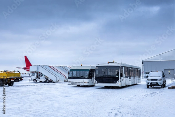 Obraz Two airport shuttle buses, empty passenger boarding stairs and other equipment on the winter airport