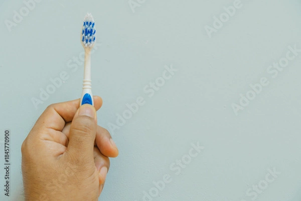 Obraz Hand holding a toothbrush, light blue background, copy space