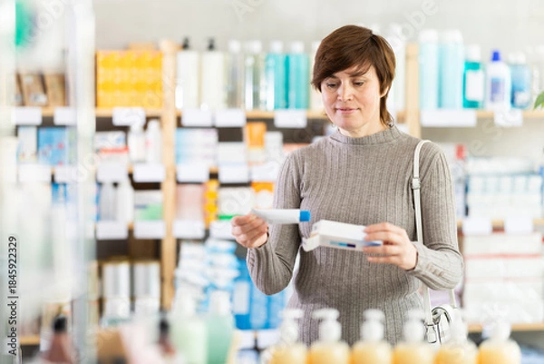 Obraz Woman in autumn clothes buys medicinal ointment at a pharmacy