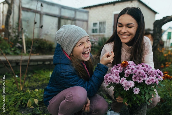 Obraz A child, a teenage girl in a garden, a vegetable garden, laughing, having fun with her mother, a young woman, with a bouquet of chrysanthemum flowers in autumn in nature.
