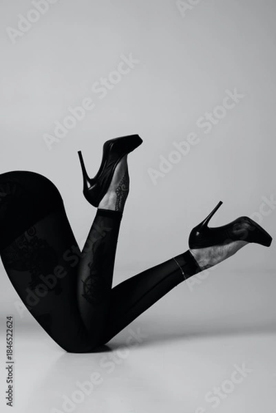 Fototapeta Elegant black high heels and patterned tights on a woman's legs in a studio setting