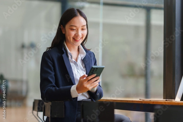 Obraz Asian businesswoman smiling, interacting with a smartphone in a modern office, representing communication and digital connectivity