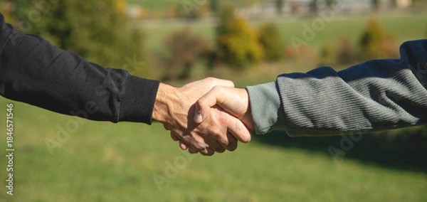 Fototapeta Two shaking hands in outdoors background.