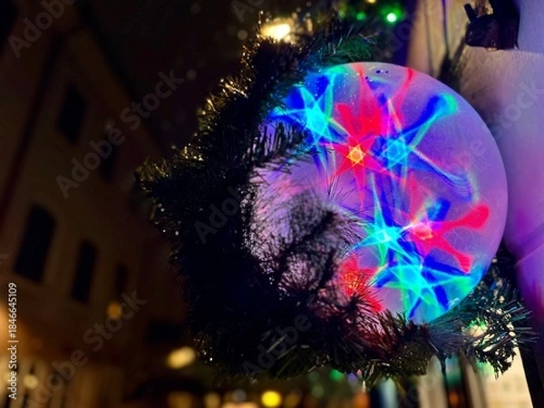 Obraz Colorful glowing spherical ball decoration against a city street with lights and bokeh. Festive atmosphere in the night urban environment. Christmas greeting card with copy space