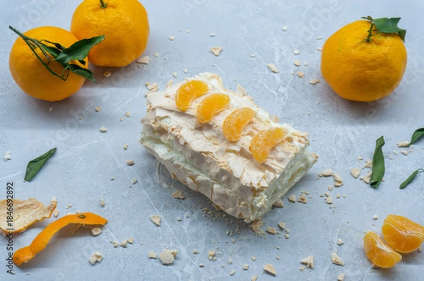 Fototapeta A delicious meringue roll with fruit. A top view of the meringue cake and tangerines against a gray background.