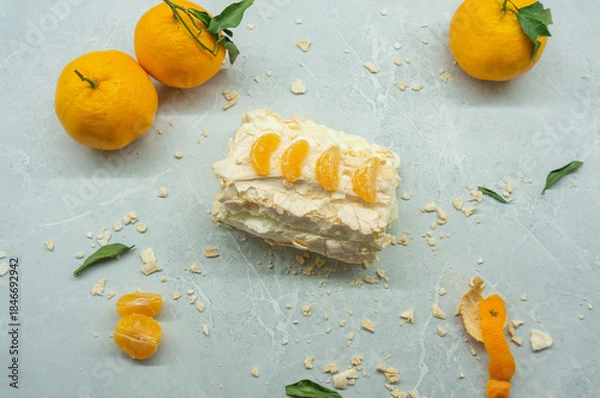 Fototapeta A delicious meringue roll with fruit. A top view of the meringue cake and tangerines against a gray background.