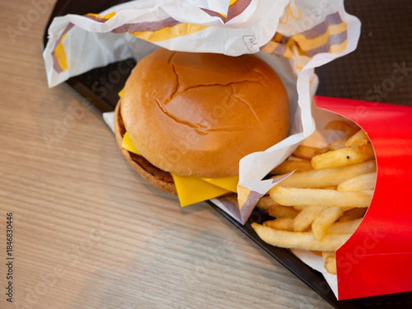Obraz Close up crispy french fries in red paper box with cheeseburger background on tray, fast food side dish and unhealthy snack concept.