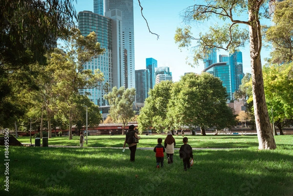 Obraz A family joyfully walking in a lush park with a vibrant city skyline backdrop