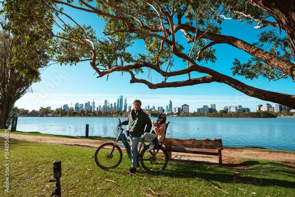 Obraz A man is riding a bike close to a beautiful scenic waterfront and city skyline