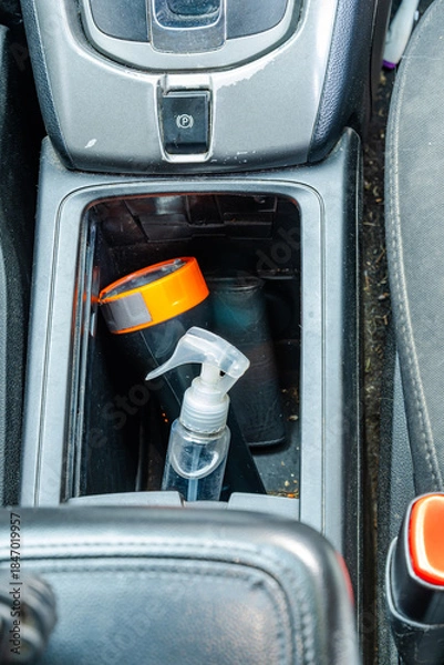 Obraz Car console with spray bottle, flashlight, and charger plug beside parking brake button.