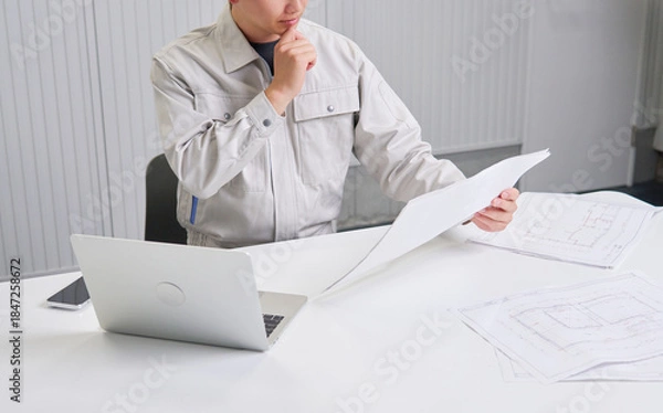 Obraz 図面を持ってデスクで考える作業員　顔無し