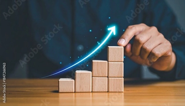 Obraz Hand building ascending bar graph with wooden blocks and a glowing upward arrow symbolizing business growth and success.