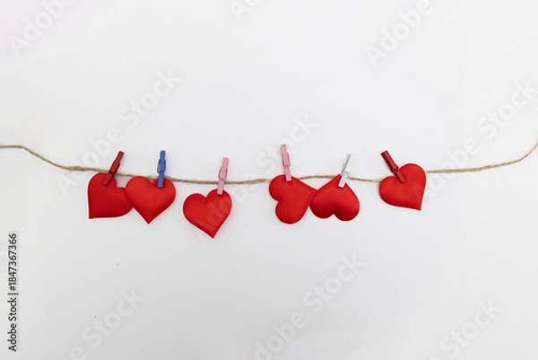 Obraz Several red heart shapes are attached to a rustic string with different colored clothespins against a plain white background. This is meant as digital content for Valentine's Day.