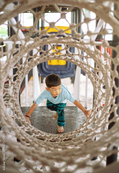Fototapeta Asian Little Boy Crawling Through Rope Tunnel Playground, Active Child Developing Motor Skills