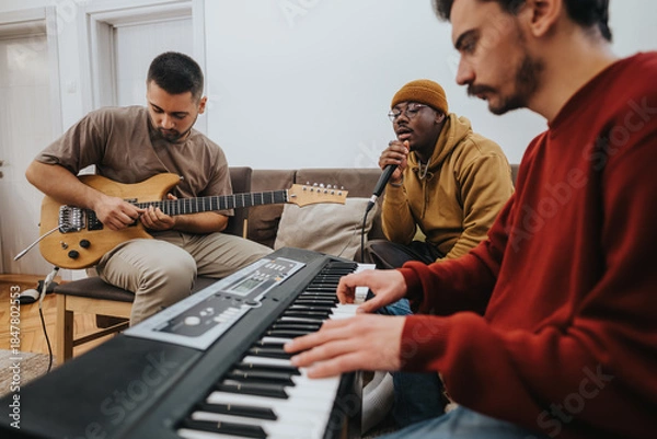 Obraz Three friends play music together in a cozy living room, with guitar, keyboard, and microphone. A casual jam session among friends captures creativity and collaboration.