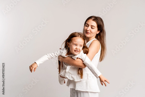 Fototapeta mother and child girl on a white cyclorama background, mother and daughter in a white suit hugging and kissing while playing, portrait, place and space for text