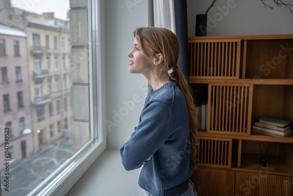 Fototapeta Dreaming woman enjoys looking at window, mindful pause at home deep in pleased thoughts. Happy young female taking break spending slow time thinking about holidays. Calmness, gratitude, contentment.