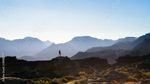 Fototapeta The silhouette of a trail runner running along a rocky mountain ridge at sunset in the mountains of South Africa
