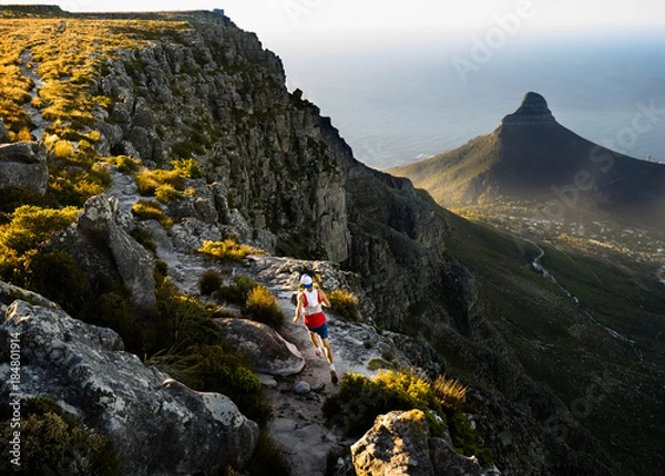Fototapeta Trail runner running along a trail on the top of Table Mountain in Cape Town while out training in the mountains at sunset