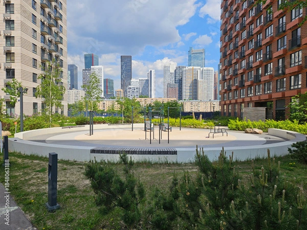 Obraz Park with a large circular area in the middle. There are benches and a few trees. The park is surrounded by buildings near entrance in the courtyard of the house in residential complex
