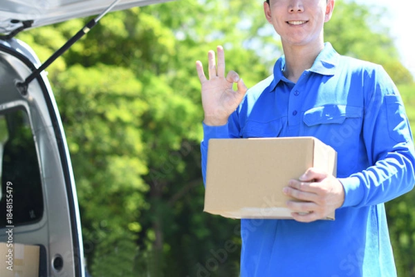 Obraz 屋外で配送スタッフが荷物を持ちOKをする