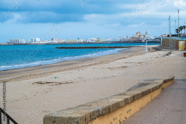 Obraz Wide sandy beach with calm sea and blue sky, coastal city on the horizon creating a peaceful seaside landscape with copy space.