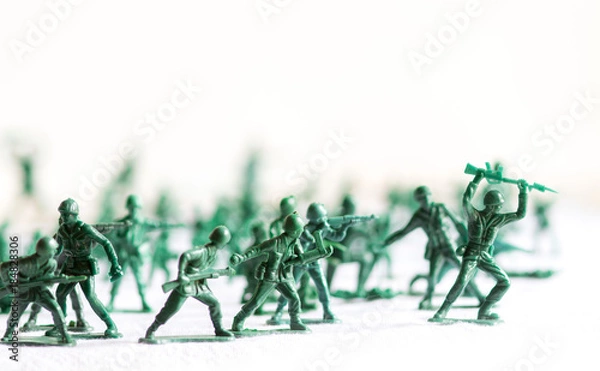 Fototapeta Many green army plastic toy soldiers organized on top of a white surface and background, isolated, with out of focus plastic soldiers in the background
