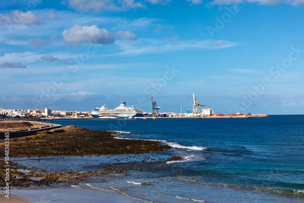 Obraz Port of Puerto del Rosario, capital of Fuerteventura in Canary Islands. Foreground features rocky coastline leading to harbor with large commercial cranes and a cruise ship docked at the pier