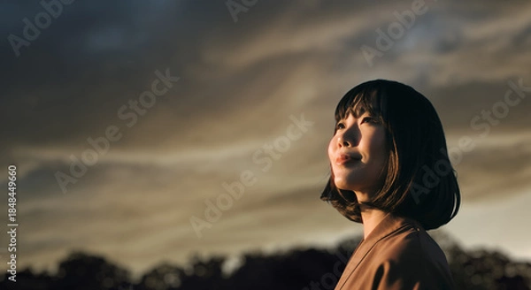 Obraz 美しい夕焼け・朝焼け　夕日・朝日に照らされた空と日の出の光を浴びた背景　空を見上げ上を向きリラックスした表情の女性の横顔　日本・旅行・観光・アウトドア・リラクゼーションの背景　希望・安堵のイメージ