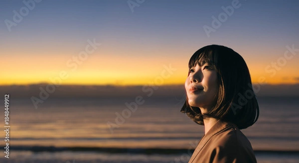 Obraz 美しい夕焼け・朝焼け　夕日・朝日に照らされた海と日の出の光を浴びた背景　笑顔で空を見上げ上を向きリラックスした表情の女性の横顔　日本・旅行・観光・アウトドア・リラクゼーションの背景　希望・安堵のイメージ　ビジネスはじまり・出勤・転職・就職