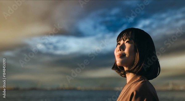 Obraz 美しい夕焼け・朝焼け　夕日・朝日に照らされた海と日の出の光を浴びた背景　笑顔で空を見上げ上を向きリラックスした表情の女性の横顔　日本・旅行・観光・アウトドア・リラクゼーションの背景　希望・安堵のイメージ　ビジネスはじまり・出勤・転職・就職