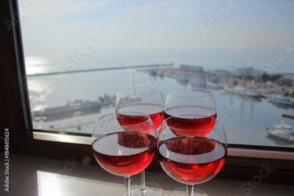 Obraz Red wine glasses by window overlooking harbor