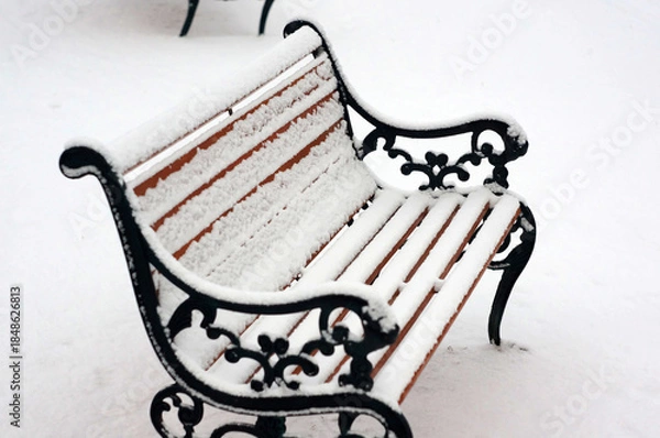 Fototapeta しんしんと降り積もる雪に覆われた公園のベンチ。静かな冬の日の屋外風景。